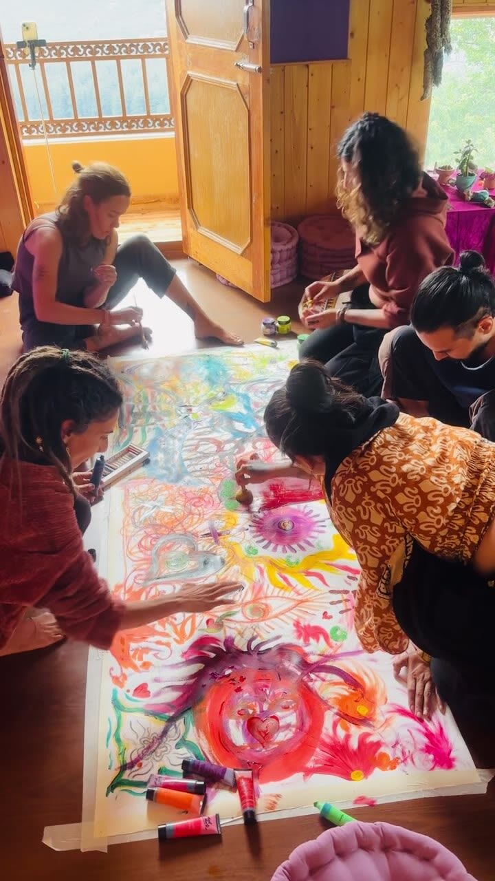 Guests kneeling around a large, colourful shared painting on the studio floor