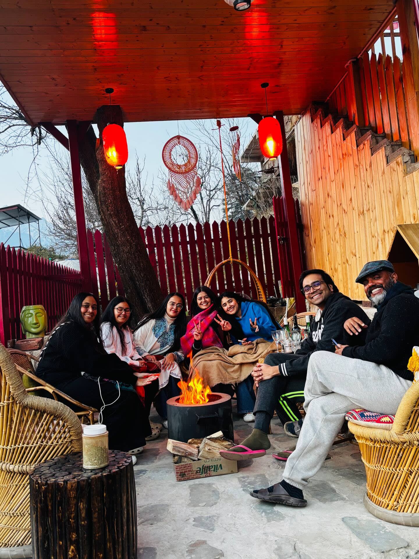 Guests sitting around a fire under the treehouse, with red lanterns and dreamcatchers