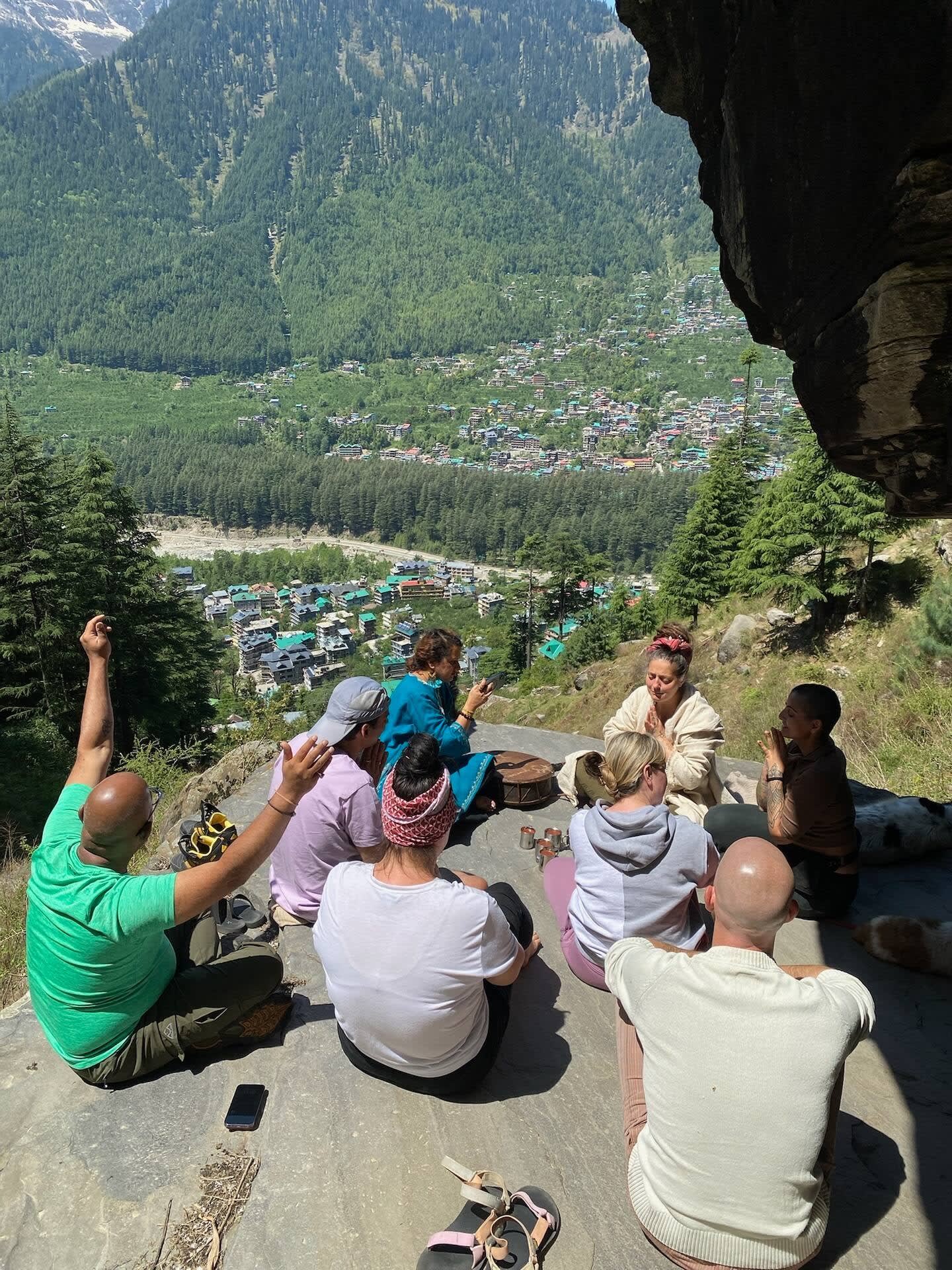A group sitting on a rock high above the valley, arms raised to the mountains