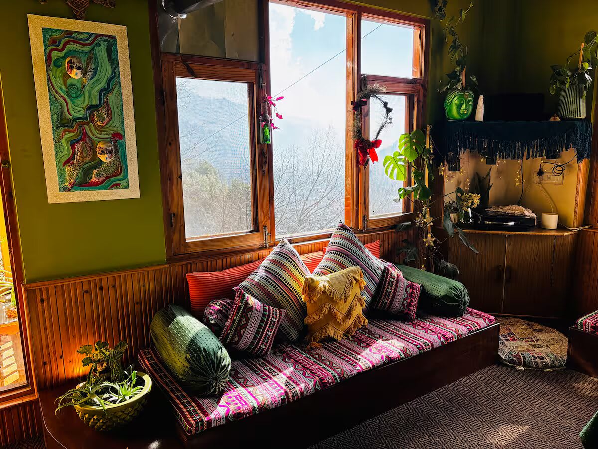 A sunny corner of the lounge: a day bed with striped cushions under wooden windows, with a painting and plants on green walls
