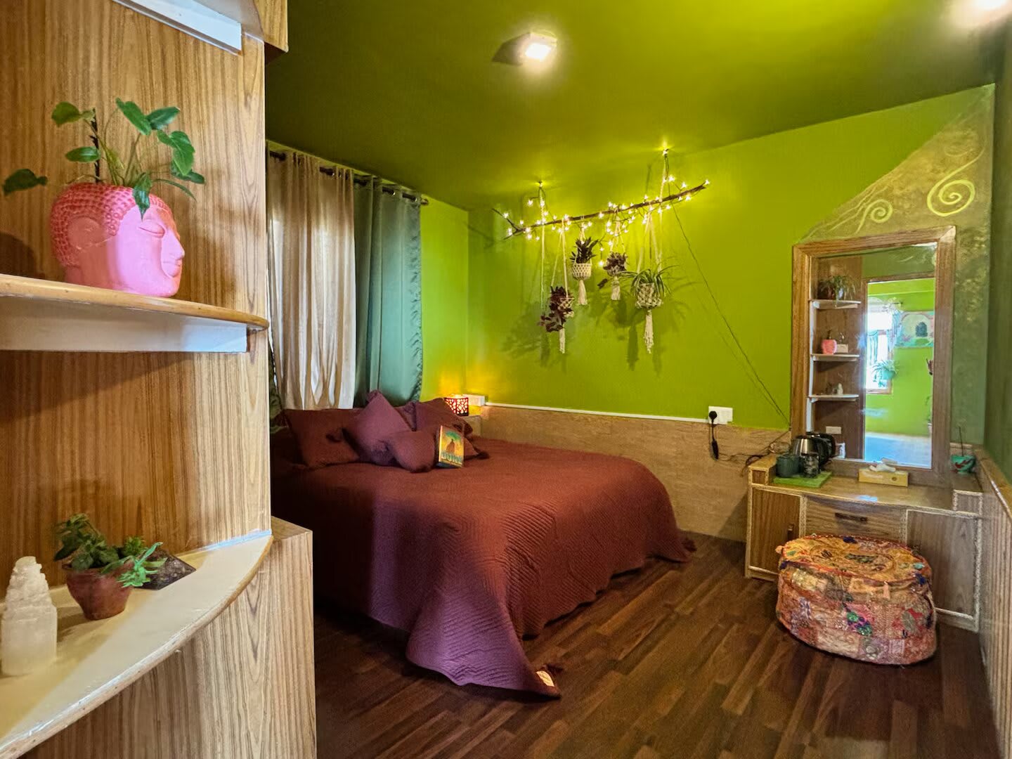 Nerika, the Green Room: a queen bed with plum bedding against bright green walls, with hanging plants, fairy lights and a dressing table