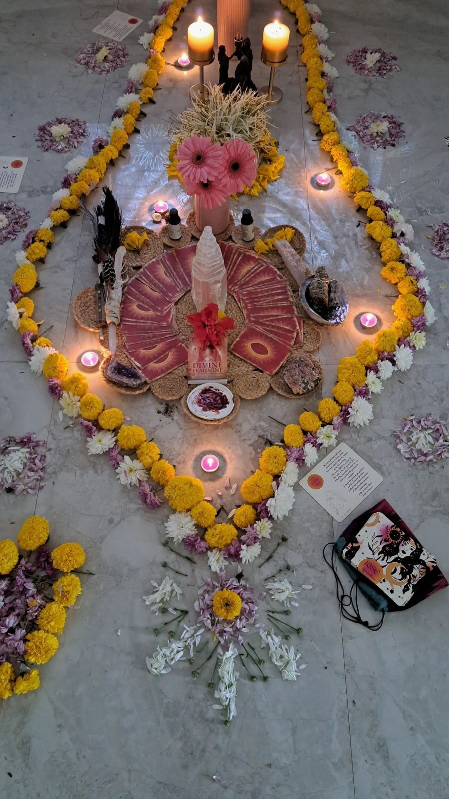 A ceremonial altar on the floor: marigolds, rose petals and candles laid out in a mandala around a central offering