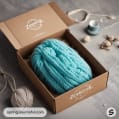 Teal yarn skein in a brown box with knitting accessories.