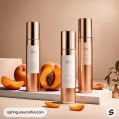 Three elegant skincare bottles in gold and white with whole and cut apricots.