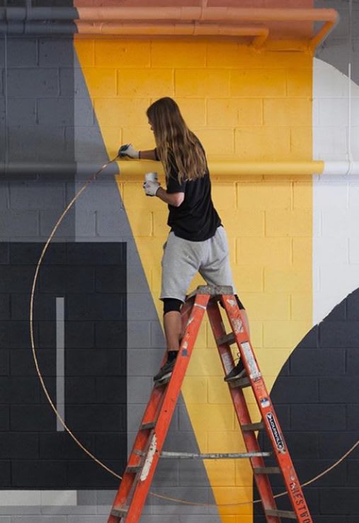 artist straddling the top of a ladder while painting a mural in a restaurant