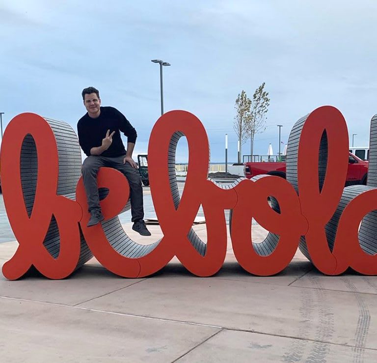 artist sitting on a sculpture that spells the words Be Bold