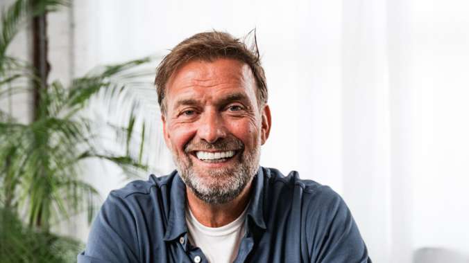 A person sitting on a brown chair and smiling. The person is Juergen Klopp.