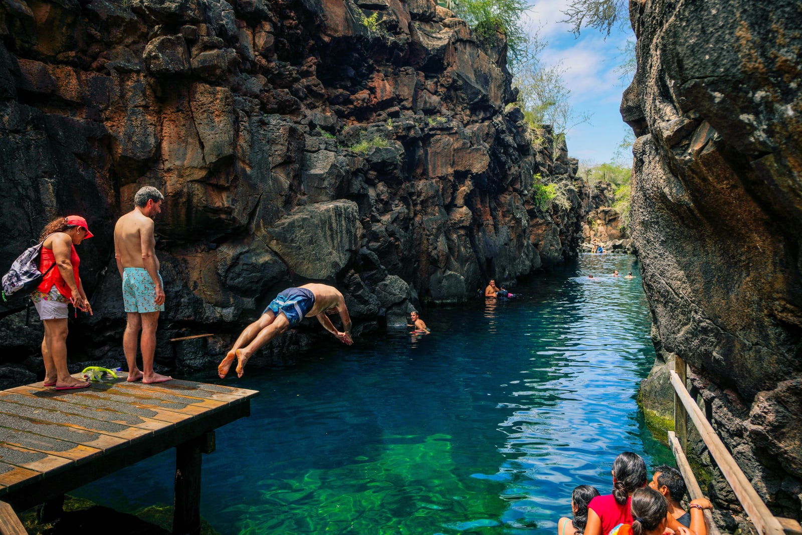 A traveler diving into a clear blue-green swimming hole cut into volcanic rock in the Galapagos