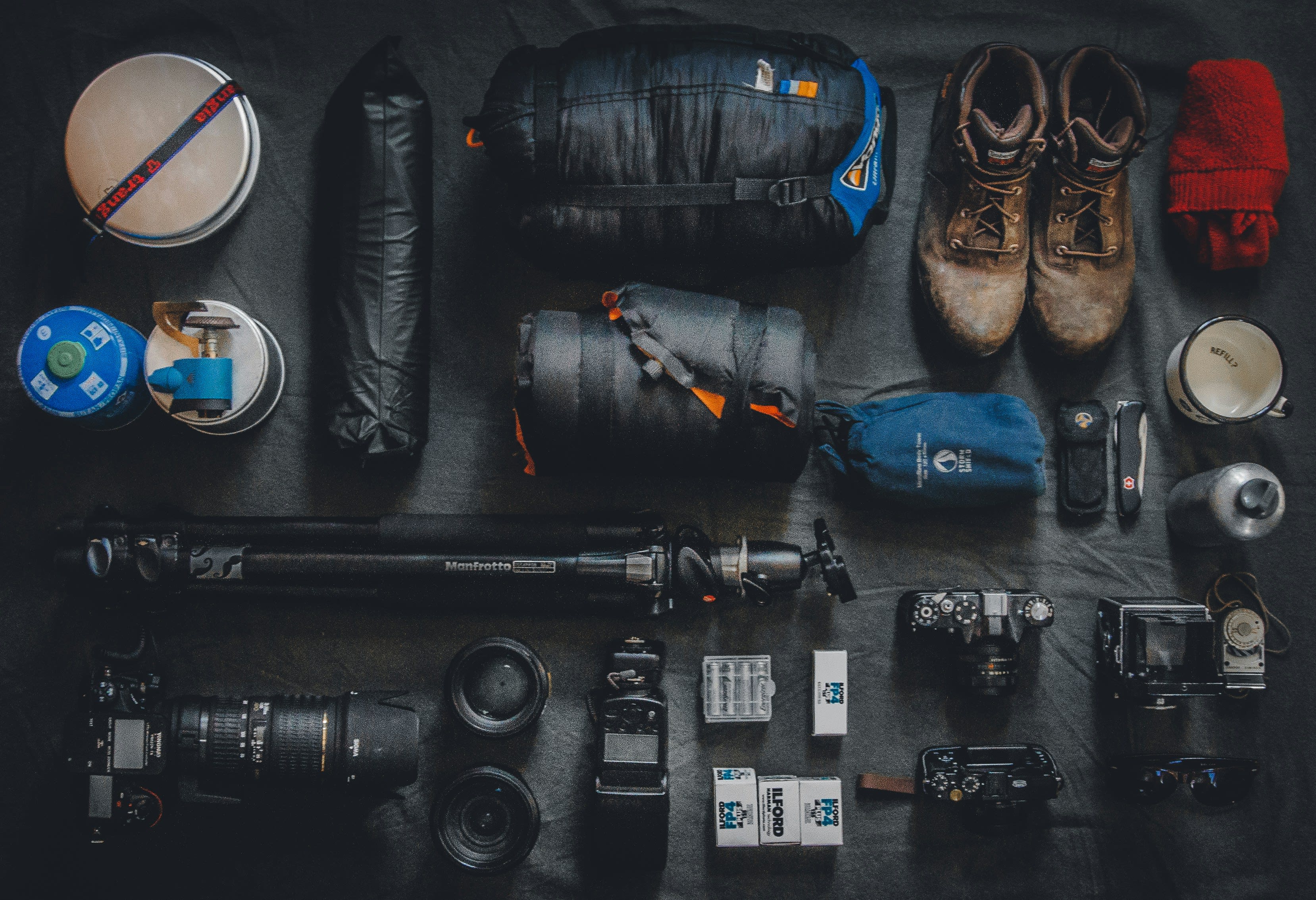 Knolling flat lay of expedition gear including sleeping bags, hiking boots, cameras, lenses, and a tripod