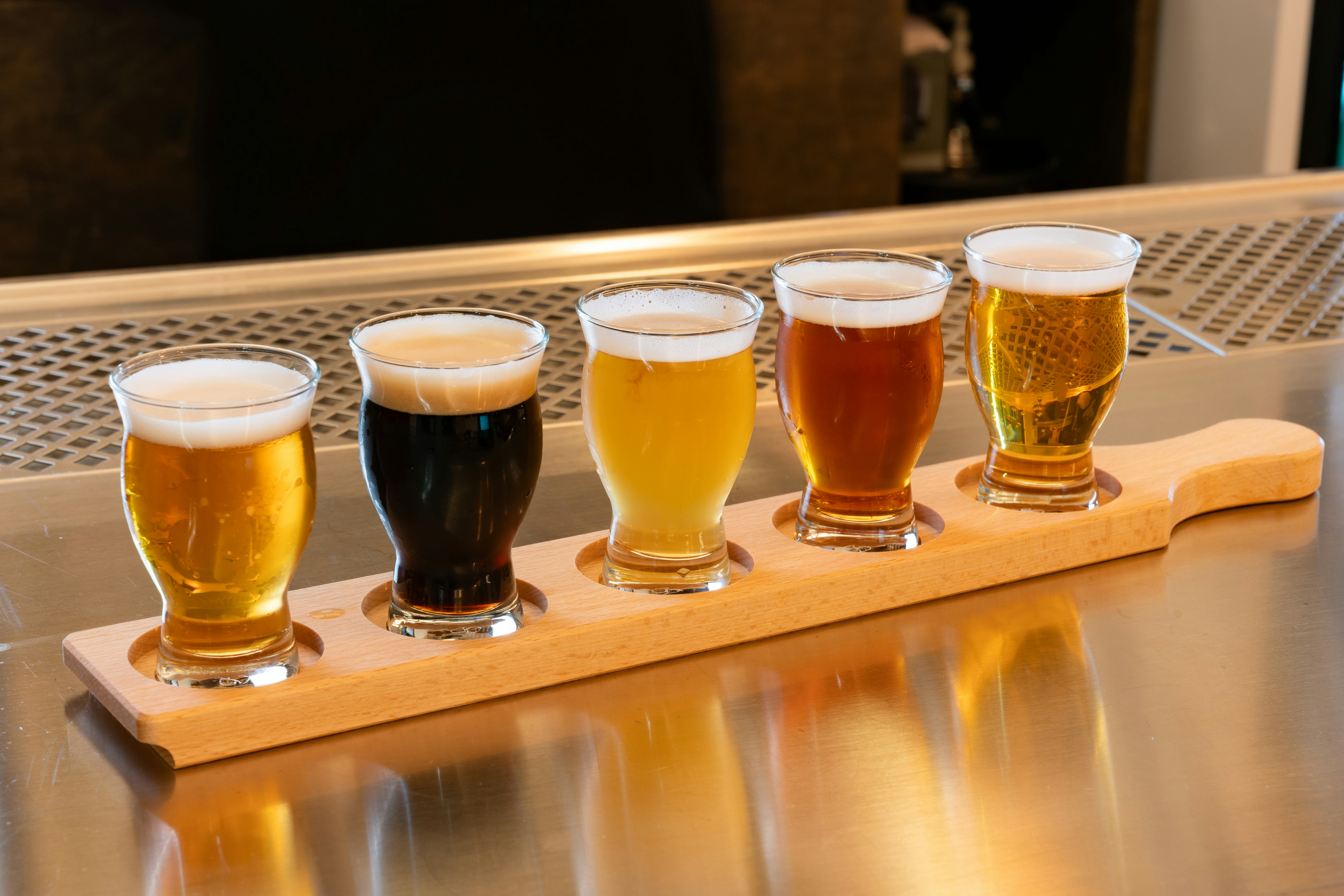 A flight of five beers in a wooden paddle on a bar counter