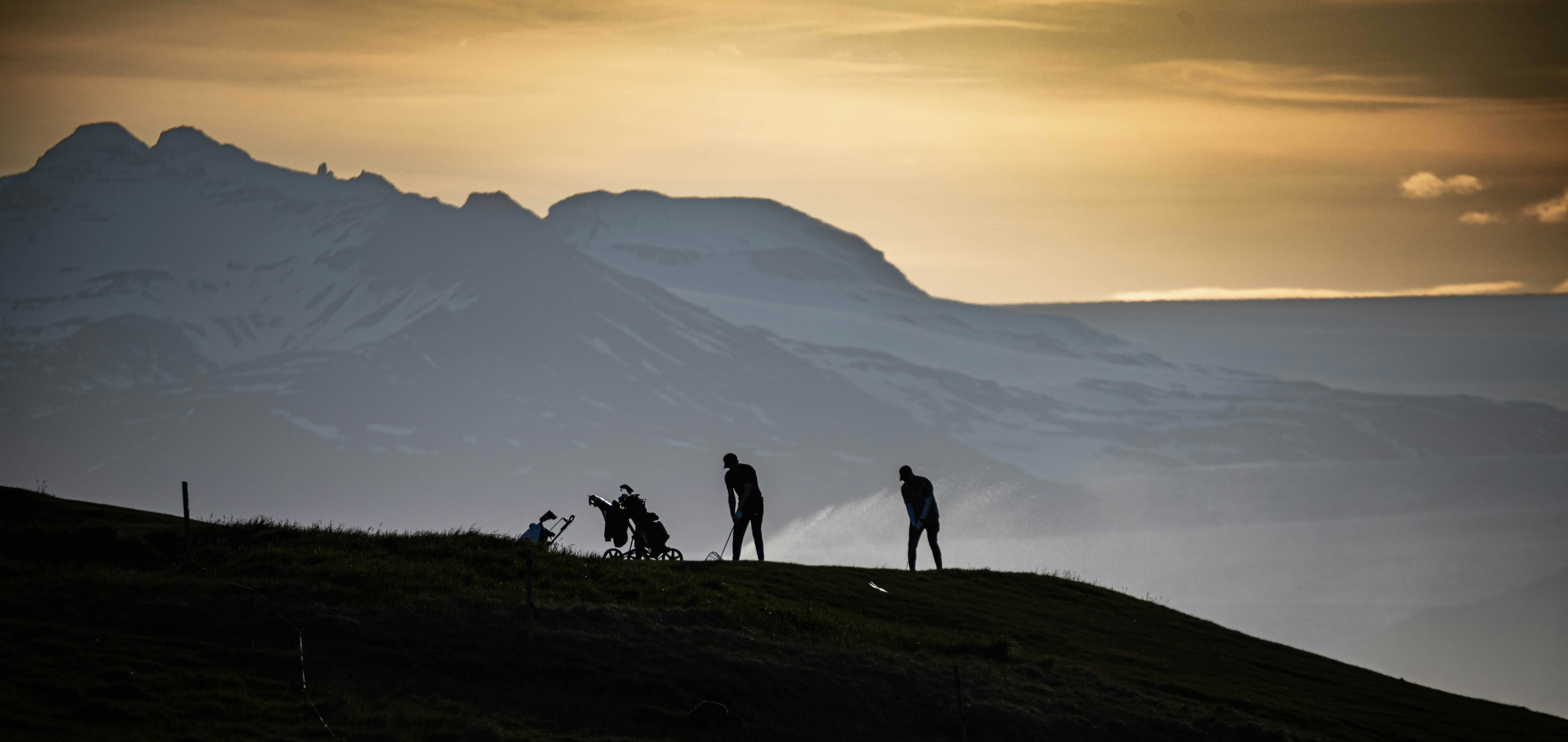 Golfers silhouetted at sunset with mountain backdrop