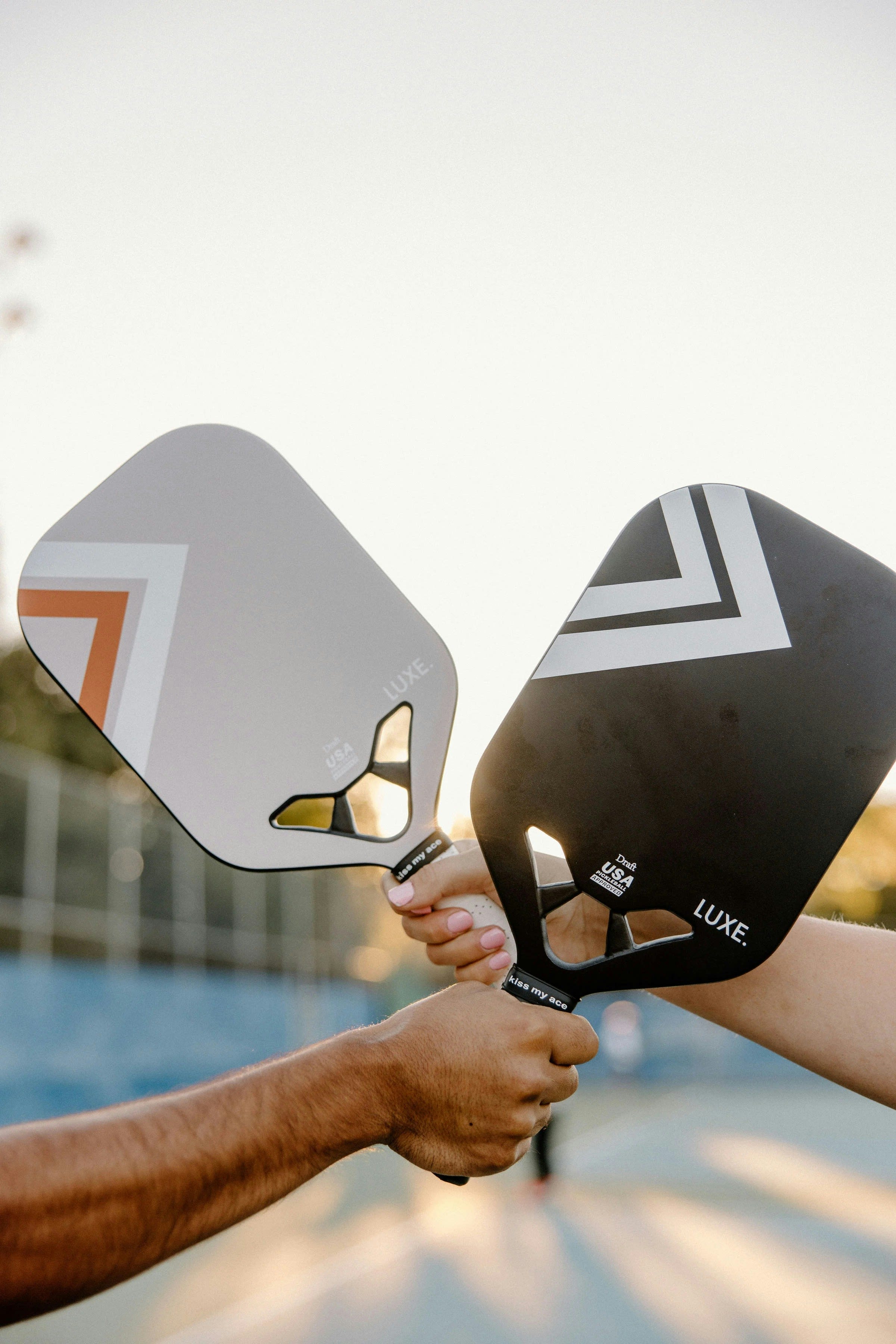 Two pickleball paddles crossing against a golden sunset sky