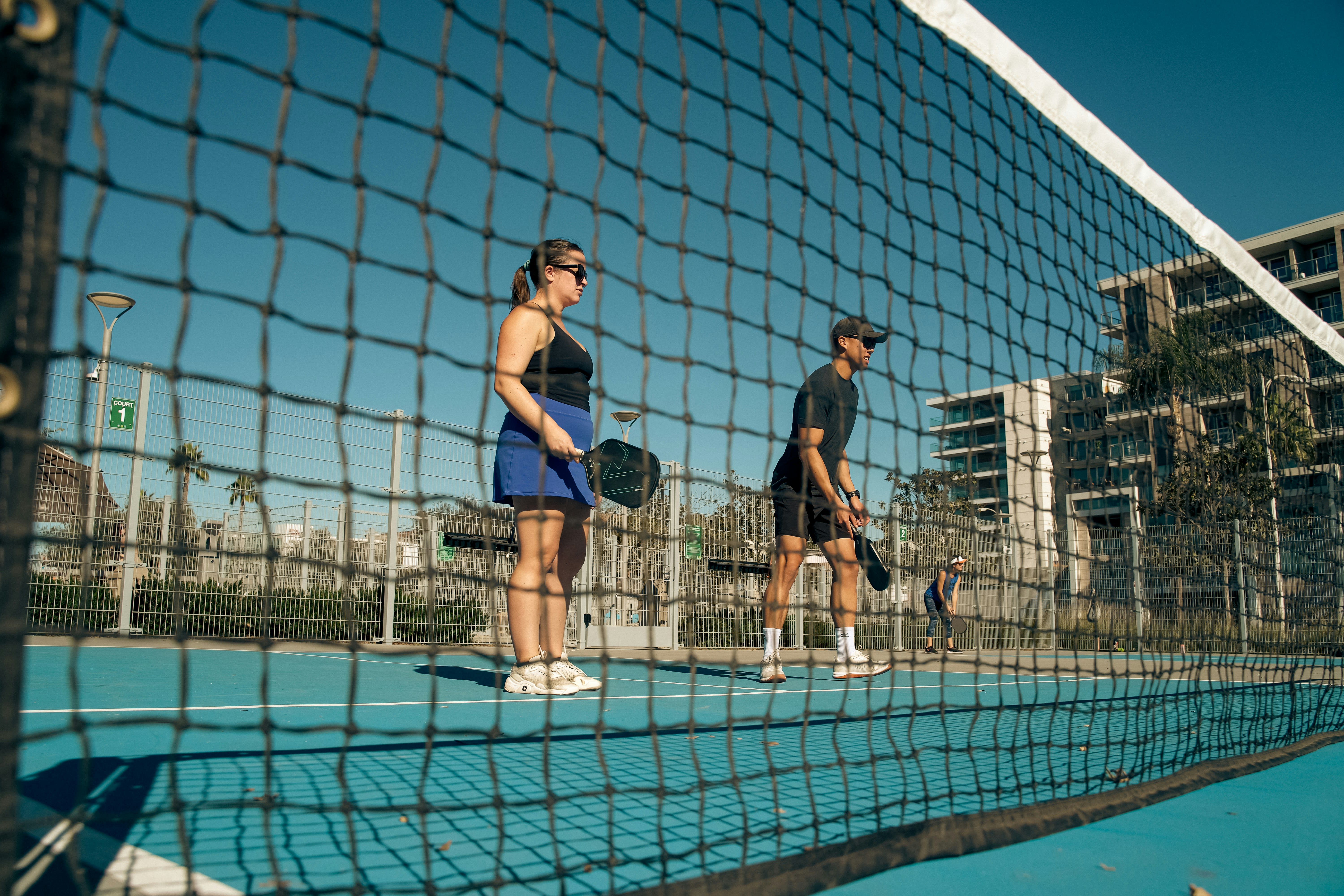 Players competing at an outdoor pickleball court with a city skyline backdrop