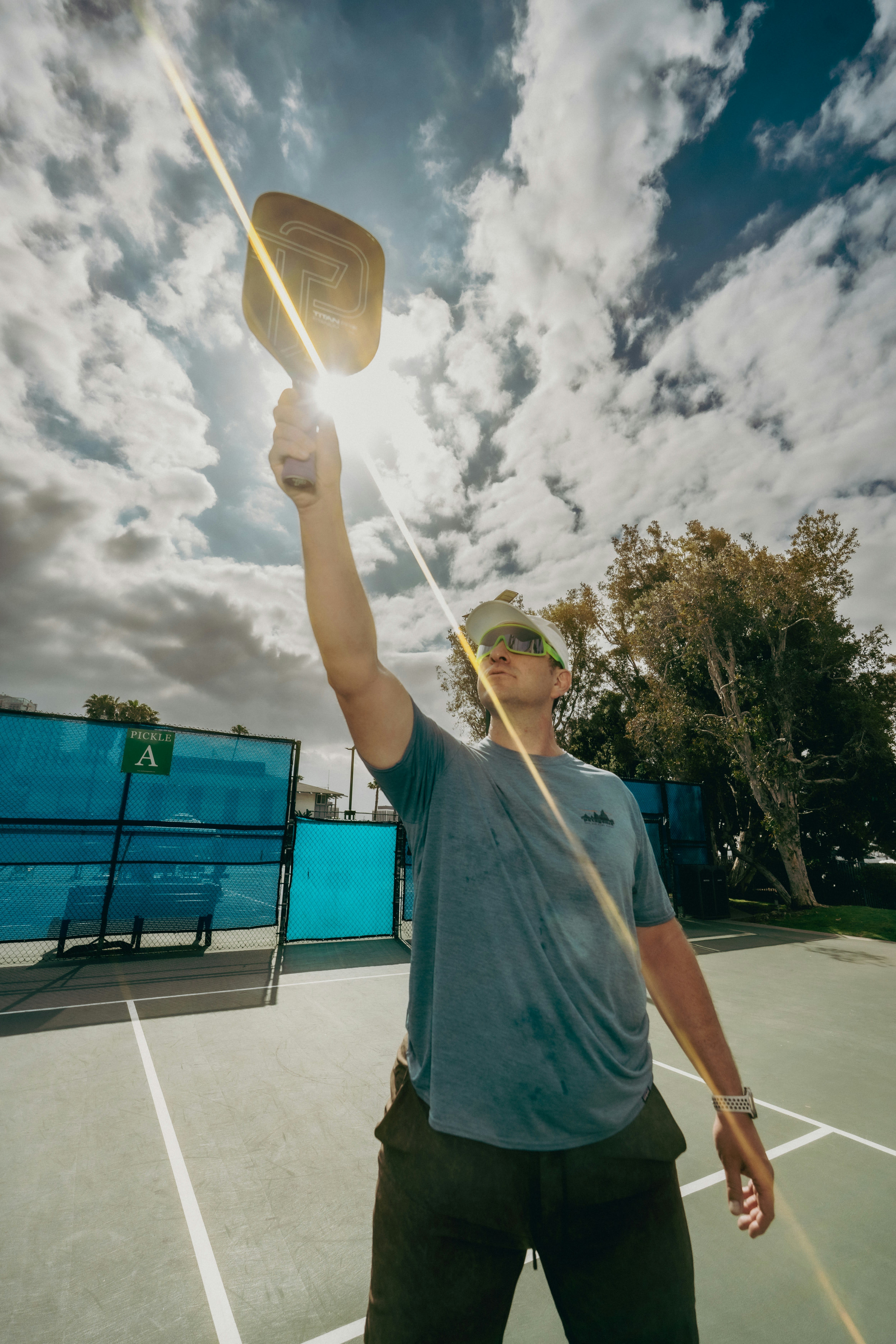Pickleball player raising a paddle dramatically against a bright sky