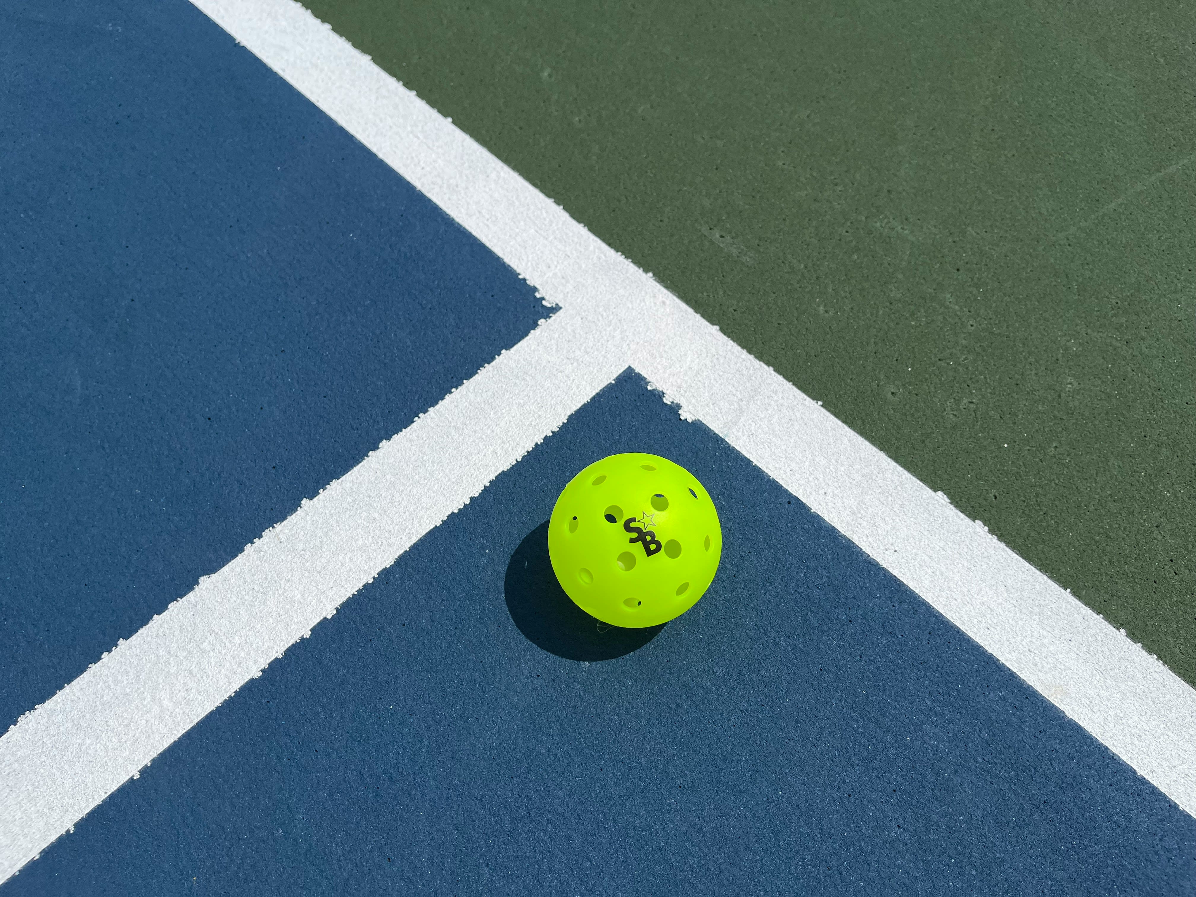 Neon yellow pickleball resting at the corner of a blue and green court