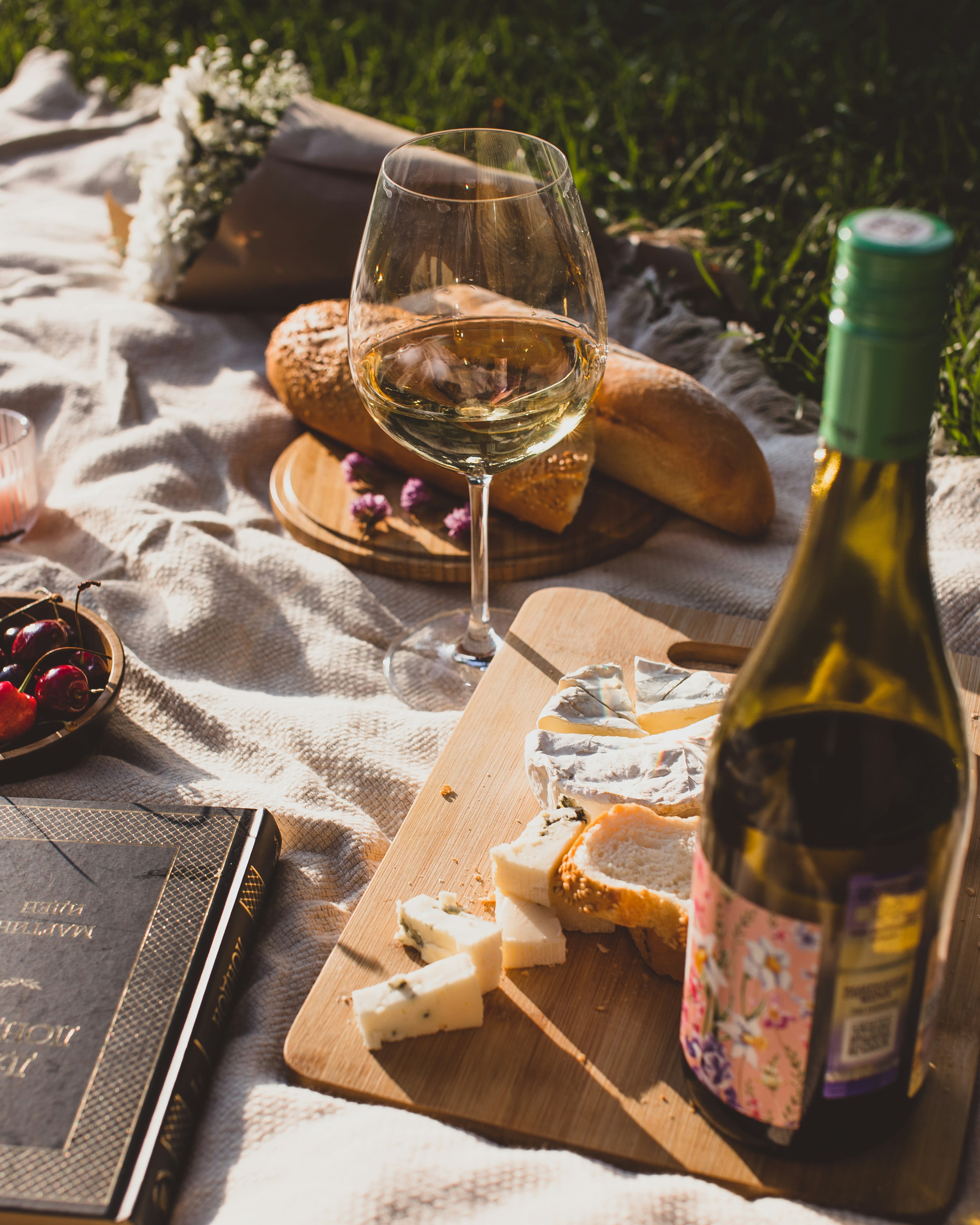 Outdoor picnic spread with white wine, baguette, and cheese