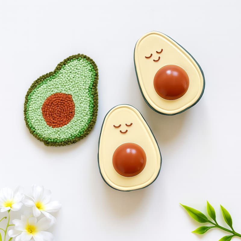 Beyaz çiçekler ve el yapımı örgü oyuncakla birlikte sunulan Hubble marka organik avokado diş kaşıyıcı seti; estetik düz zemin (flatlay) fotoğrafı.