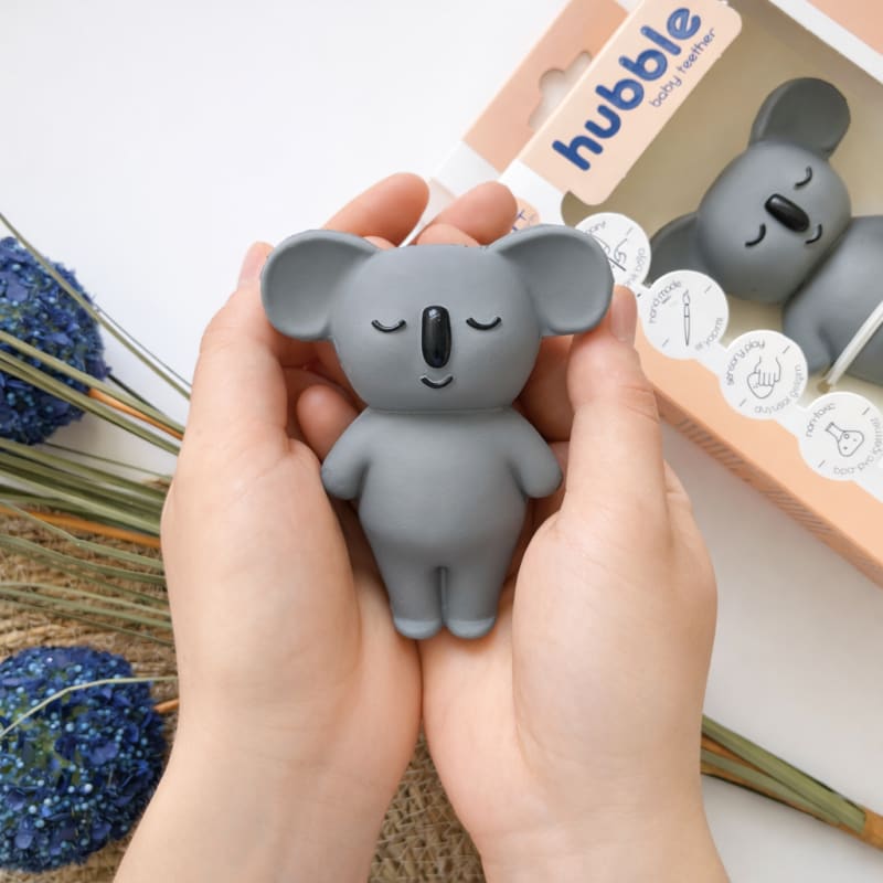 İki el arasında sevgiyle tutulan Hubble marka gri koala diş kaşıyıcı; arka planda orijinal kutusuyla ideal bebek hediyesi sunumu.