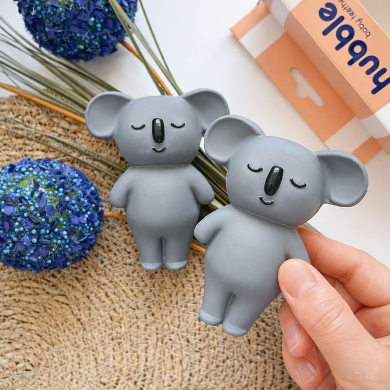 Mavi çiçekler ve hasır dekor eşliğinde sunulan sevimli koala bebek oyuncağı ve diş kaşıyıcı konsept fotoğrafı.