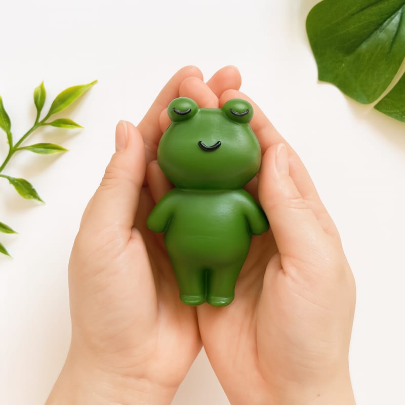 İki avuç arasında güvenle tutulan tüm vücut yeşil kurbağa figürlü doğal kauçuk bebek oyuncağı; yumuşak dokulu banyo ve diş kaşıma arkadaşı.