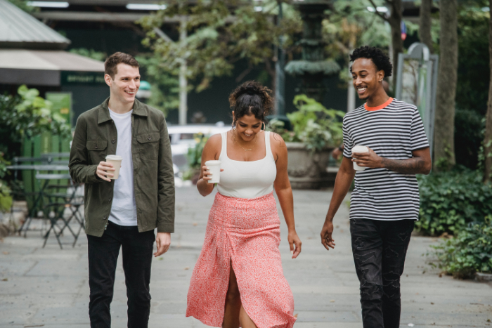 Three friends walking and chatting with coffee.