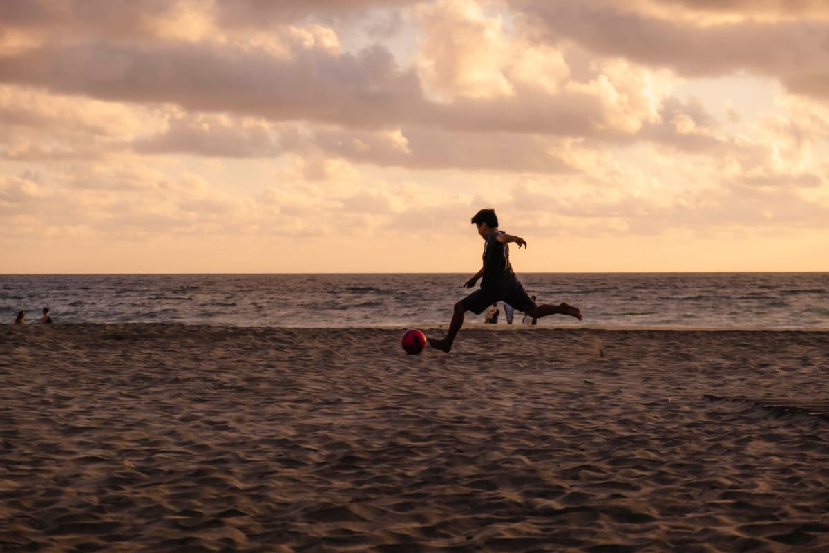 A boy kicking a ball on a wide sandy beach on the Oaxaca coast at sunset