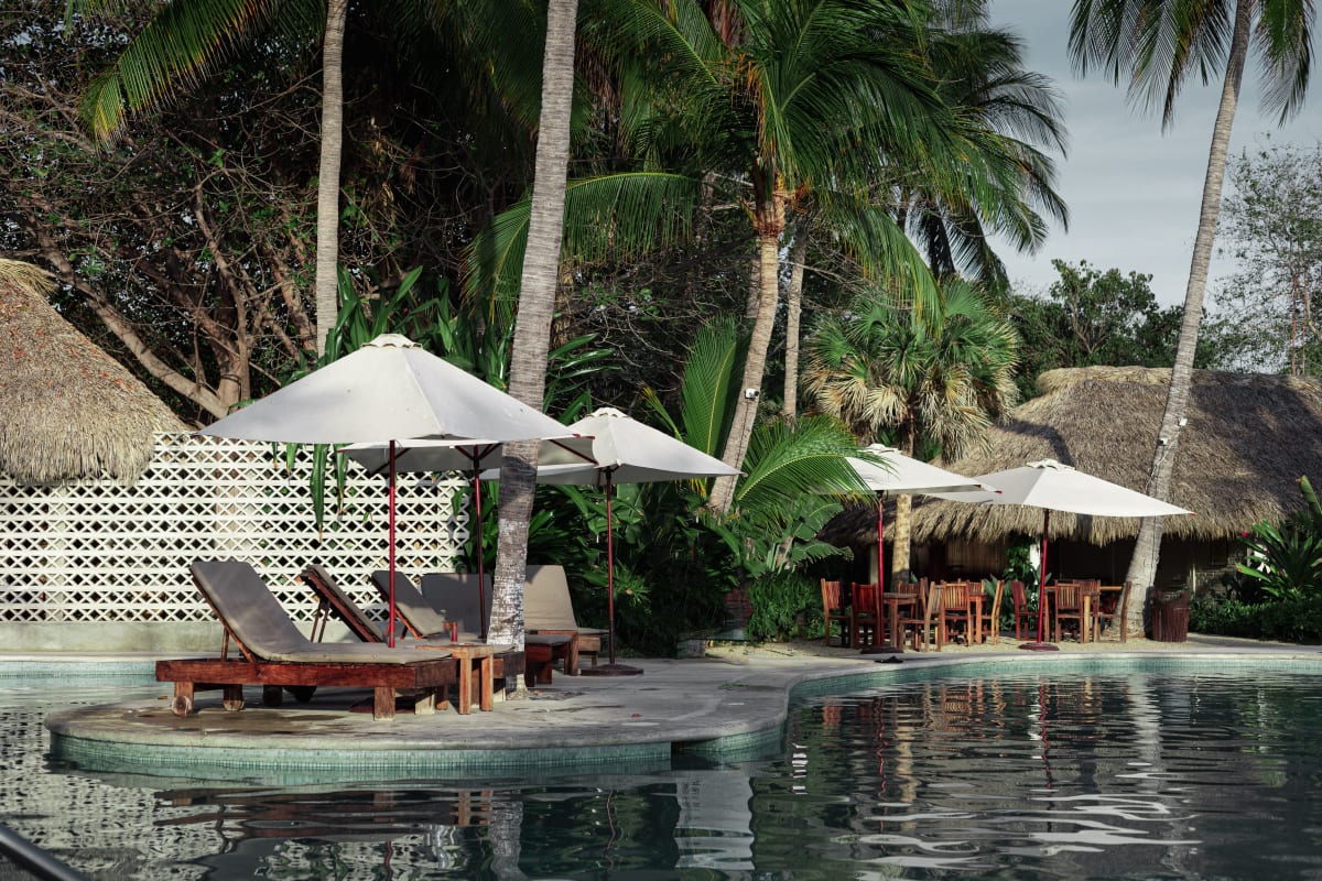 A poolside with lounge chairs and umbrellas beside palm trees in Puerto Escondido, Mexico