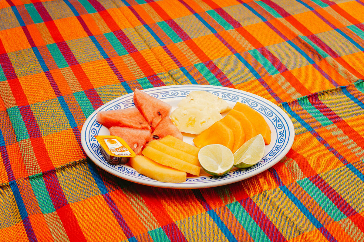 Plate of cut watermelon, papaya, pineapple and lime on a striped Mexican tablecloth