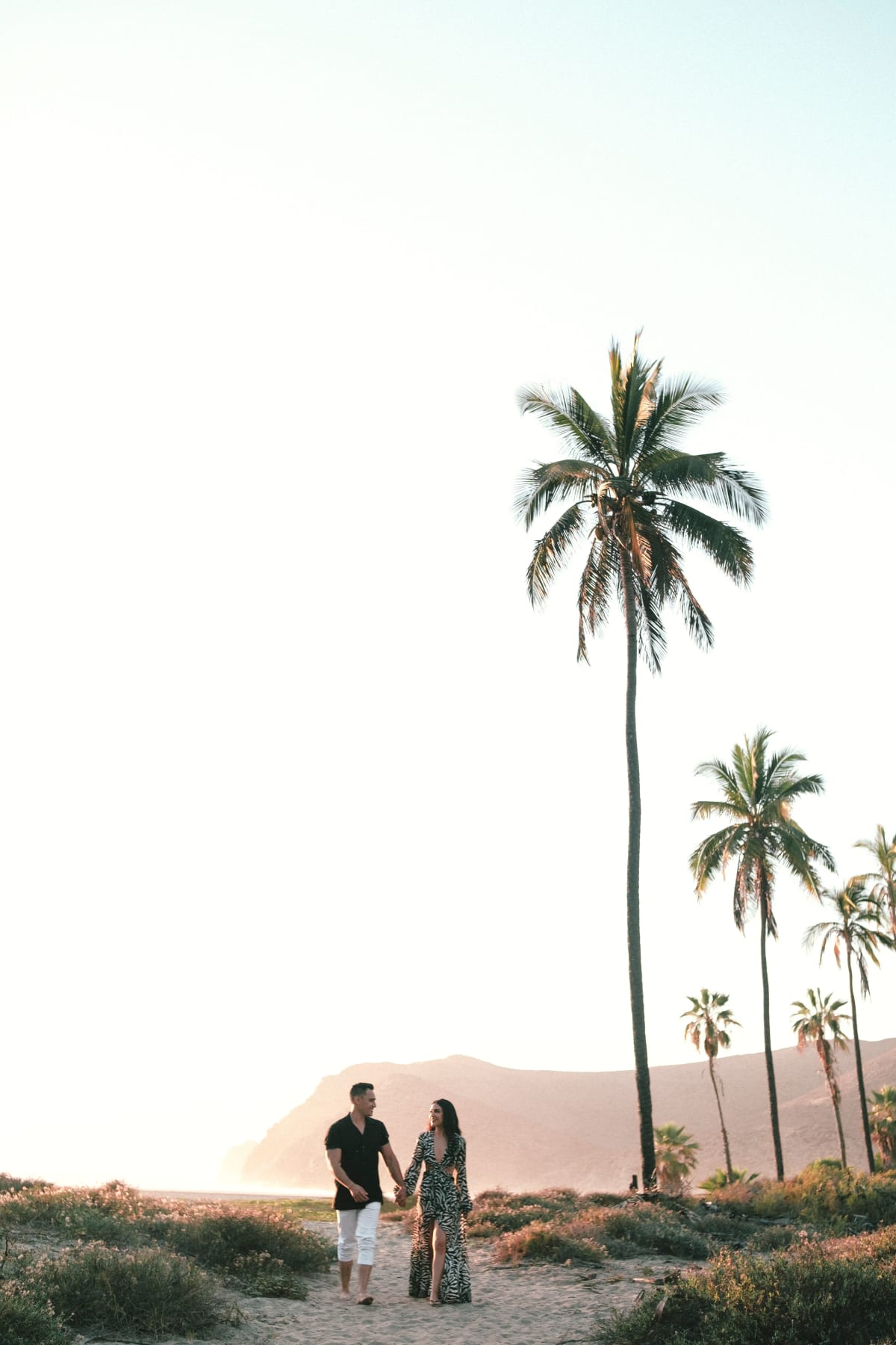 American couple walking hand in hand on a Puerto Escondido beach at sunset, part of the growing wave of Americans moving to Puerto Escondido, Oaxaca, Mexico