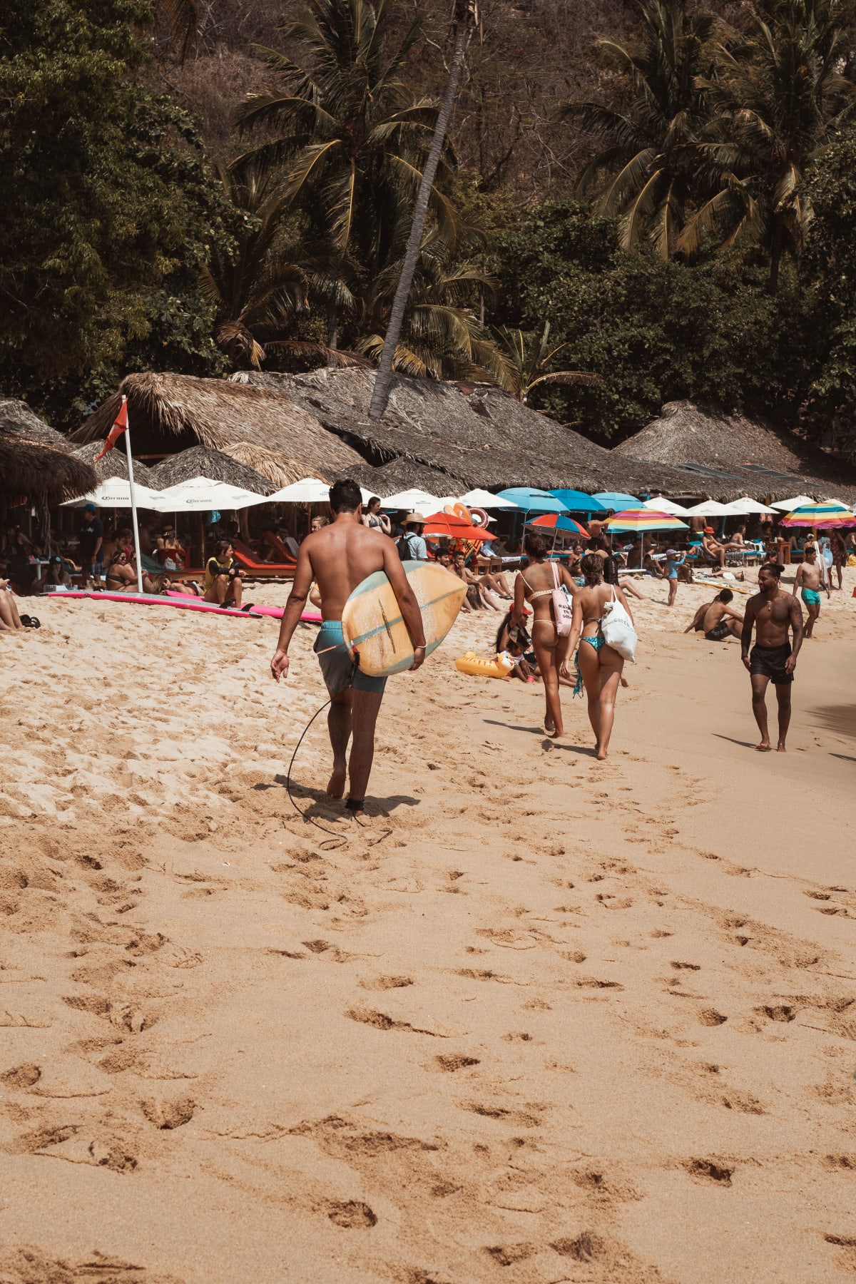 Playa concurrida en Puerto Escondido, Oaxaca con surfista dirigiéndose al océano — inversión inmobiliaria de estilo de vida