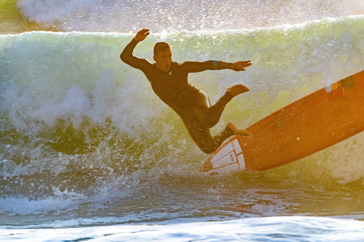 Surfista cargando tabla en playa de Puerto Escondido Oaxaca México al atardecer — el estilo de vida que lleva a surfistas a comprar propiedad