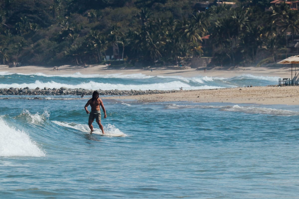 Surfer riding a wave at a sandy tropical beach near Puerto Escondido, Oaxaca — the lifestyle drawing surf-focused American expats to La Punta