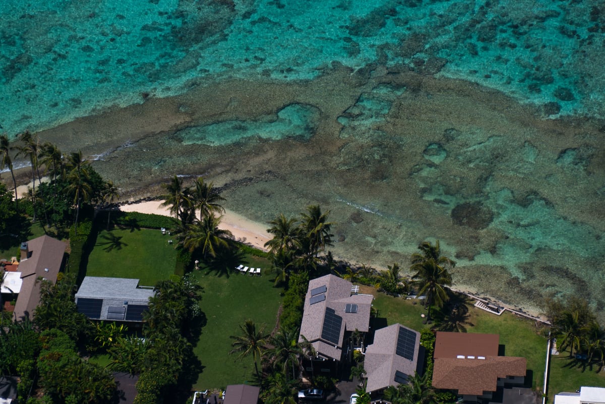 Bienes raíces sustentables Puerto Escondido — vista aérea de casas costeras con paneles solares y palmeras junto al agua turquesa del Pacífico