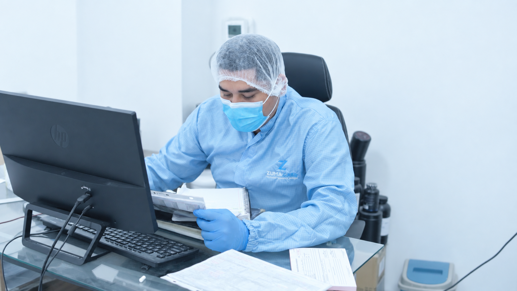 Persona en bata y cofia trabajando en la computadora durante el desarrollo de una fórmula
