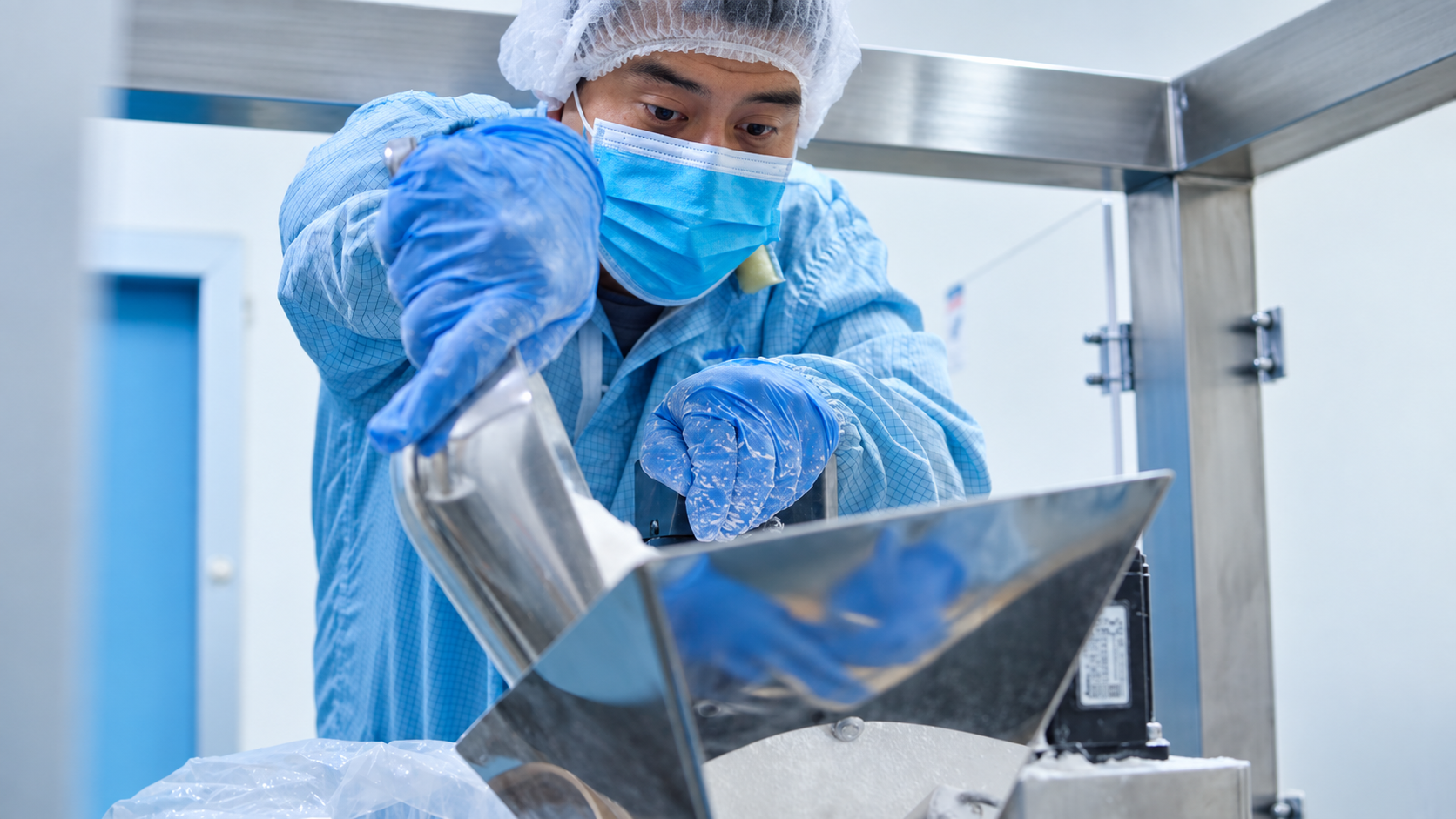 Integrante del equipo de Zuma Labs con cofia, cubrebocas y guantes vertiendo polvo en la tolva de acero inoxidable de una máquina
