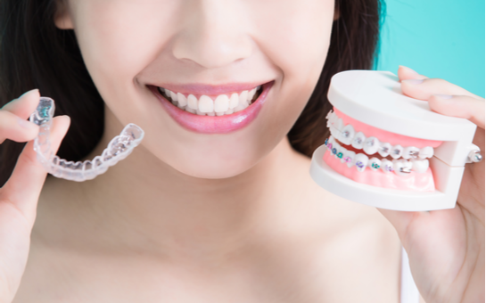 woman holding out a clear aligner and a dental model with braces