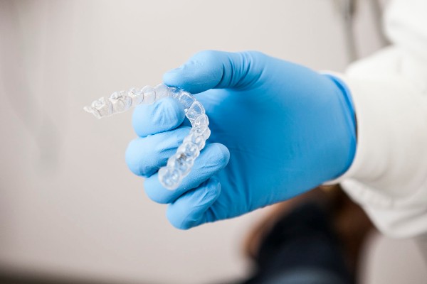 a gloved hand holding up invisalign aligners