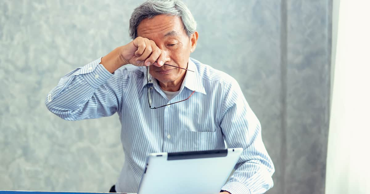 an old man rubbing his eyes while reading