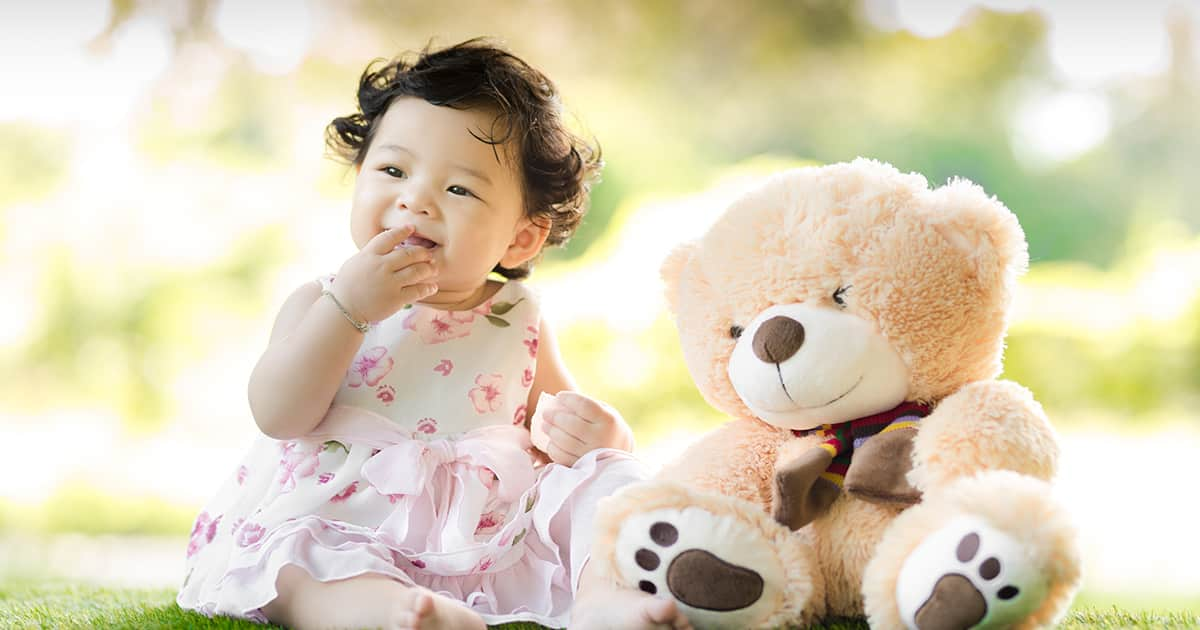 a happy baby with a teddy bear on grass