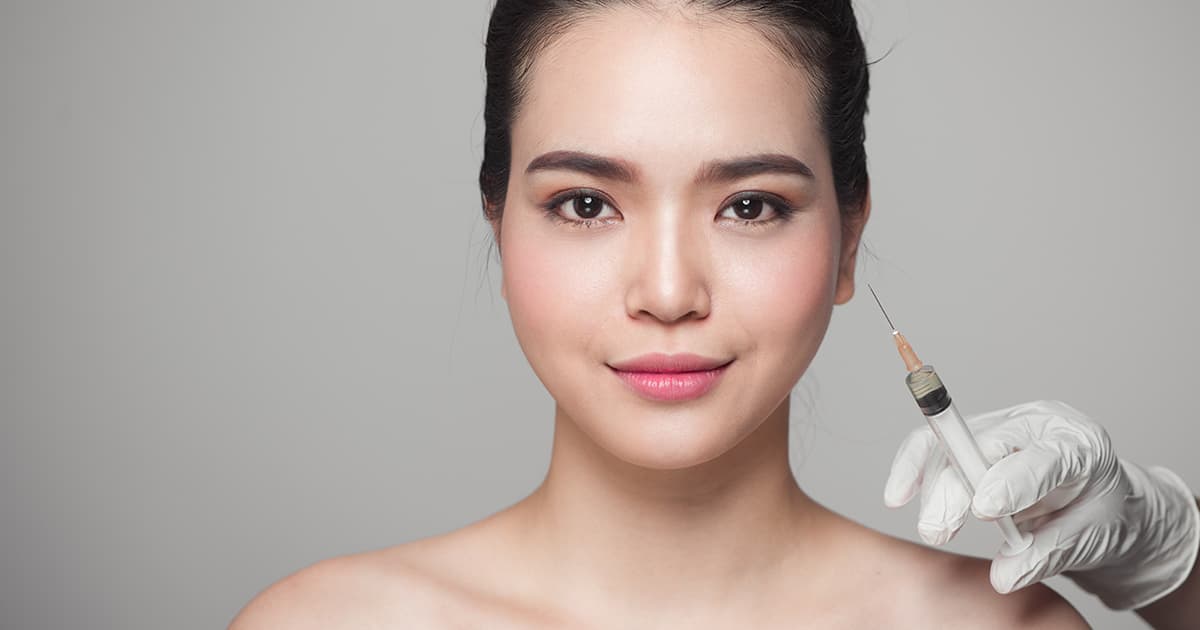 a woman smiling at the camera with a needle pointed at her face