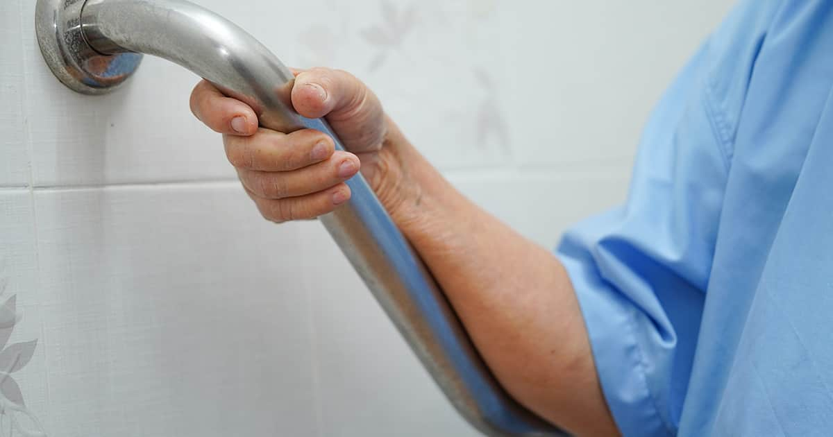 an elderly lady holding on to a grip rail in a toilet