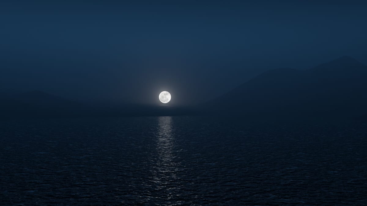 Full moon rising over a calm sea and lighting a bright path on the water at night