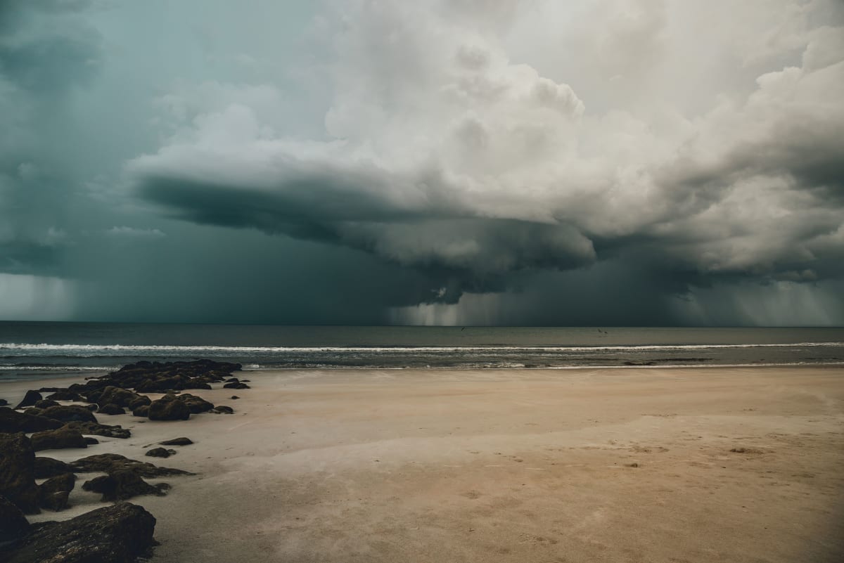 Dark storm cloud with rain falling over the sea beyond a quiet sandy beach