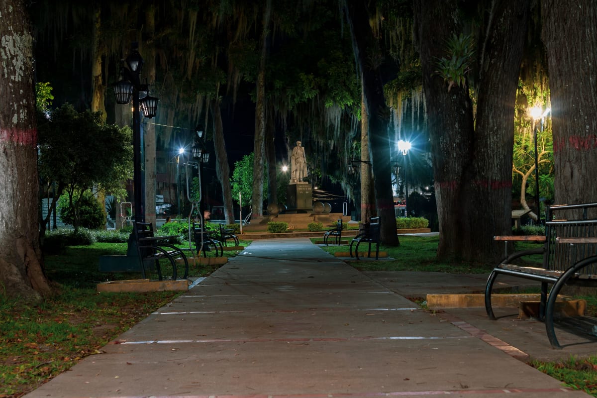 Un parque de Mérida de noche con andadores iluminados, bancas y una estatua, la vida diaria al mudarse a Mérida