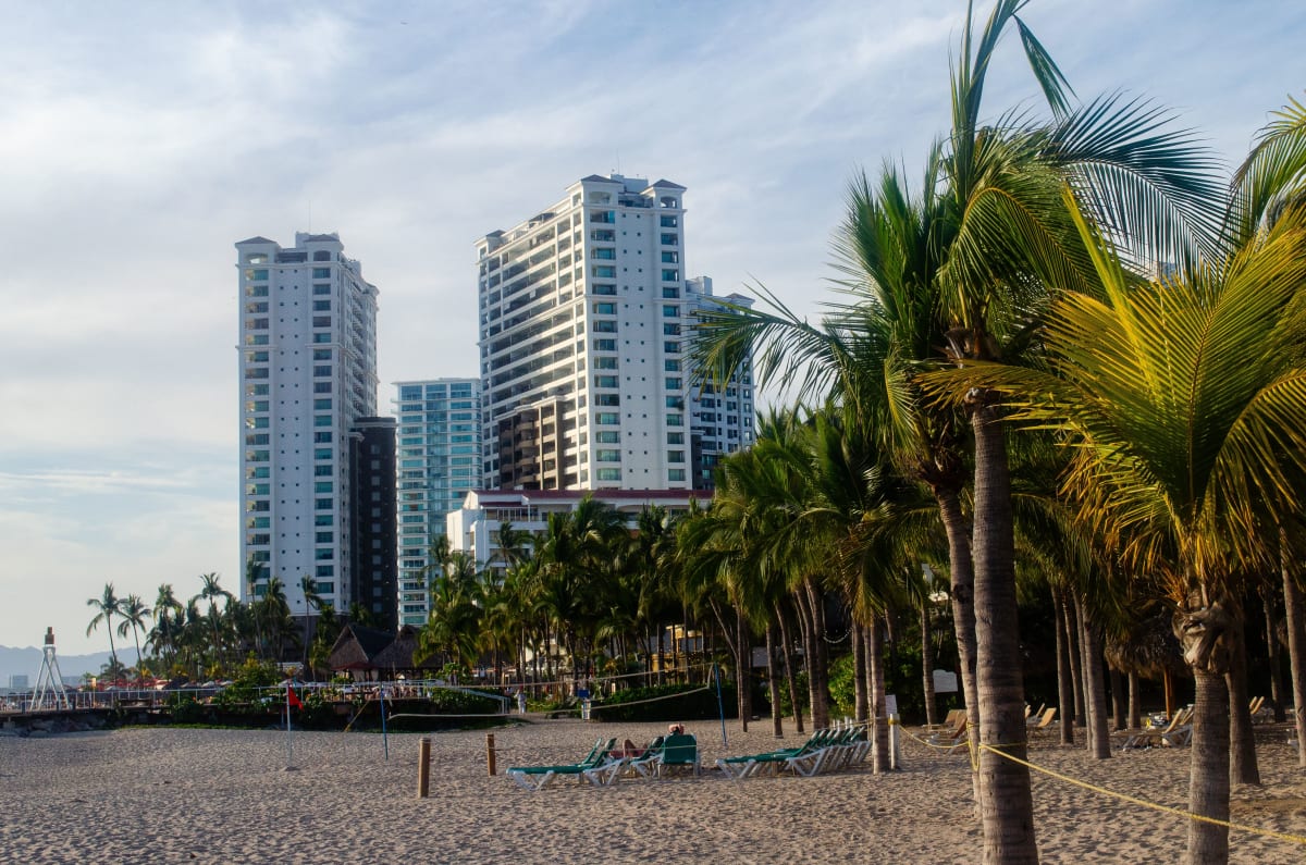 Beachfront condo towers and palm trees behind sun loungers in the Puerto Vallarta Hotel Zone
