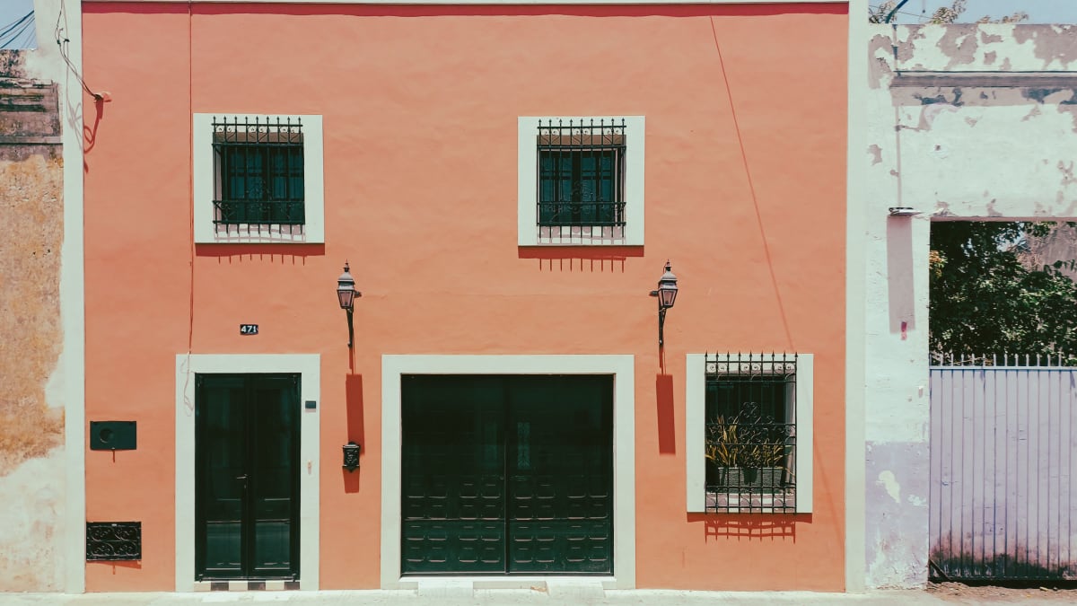 Coral-painted colonial house facade with green doors and iron window grilles in the historic center of Merida