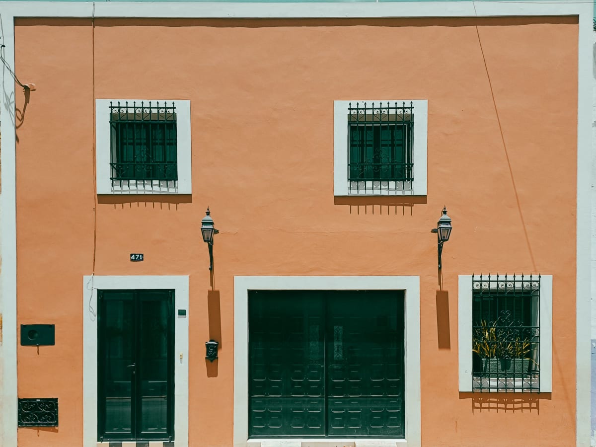 Orange colonial house front with green doors and iron window grilles in central Merida