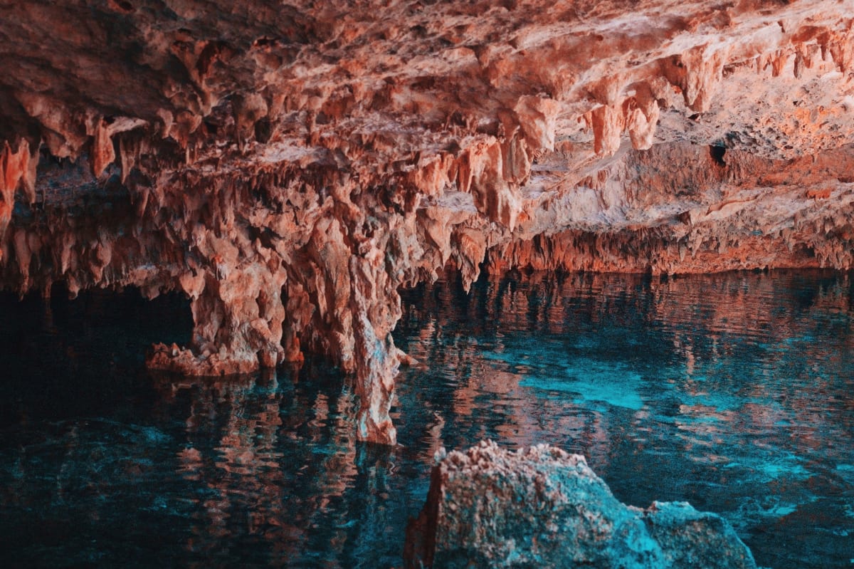 Stalactites reflected in the clear blue water of a cave cenote, the kind of underground pool found near Merida