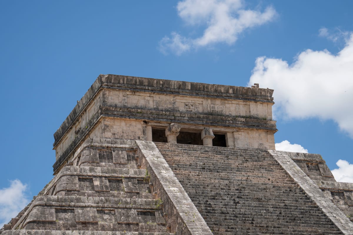 Steps and temple of El Castillo pyramid at Chichen Itza under a blue sky, a day trip from Merida