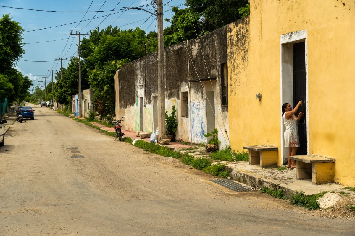 Femme à la porte d’une maison jaune dans une rue résidentielle calme de Suma, un village de l’État du Yucatán